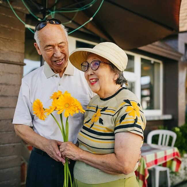 An elderly Asian couple smiles holding yellow flowers. They are ready for their retirement in Las Vegas